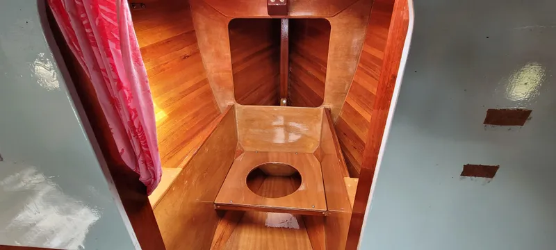 Slide: The Image of Wooden interior of 2009 Golant Gaffer Cutter Rig boat, featuring a simple wooden toilet. - 13