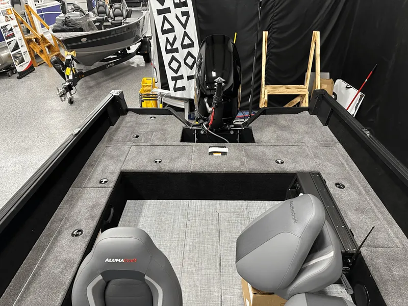 Slide: The Image of 2025 Alumacraft Competitor 185X Tiller boat interior with seating and motor, displayed indoors. - 13