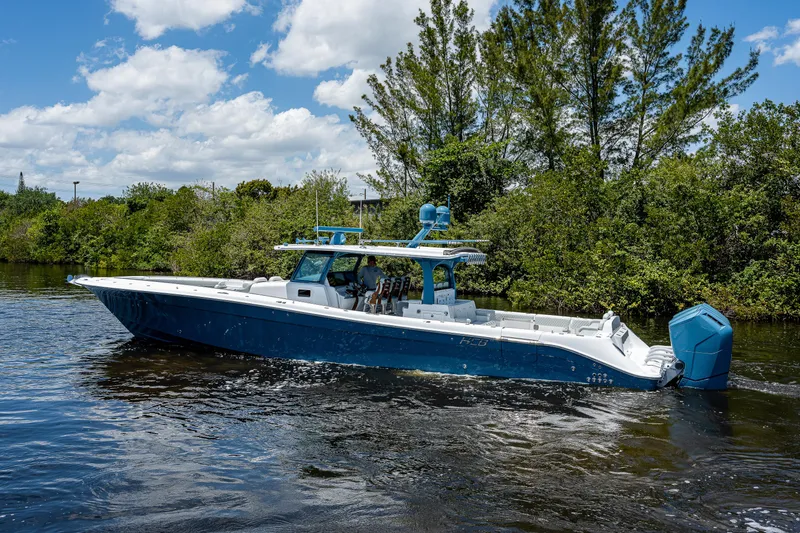 Slide: The Image of 2023 HCB 53 Sueños boat cruising on a sunny day, surrounded by lush greenery. - 2