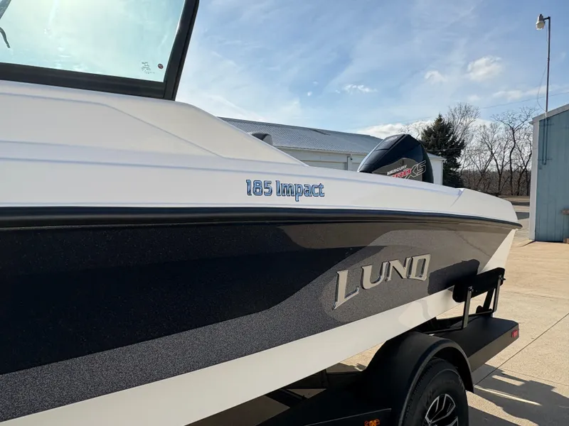 Slide: The Image of 2025 Lund 185 Impact GL boat, sleek design, parked outdoors on a sunny day. - 10
