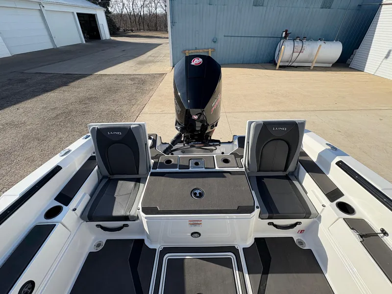 Slide: The Image of 2025 Lund 185 Impact GL boat interior with seating and motor, parked outdoors. - 34