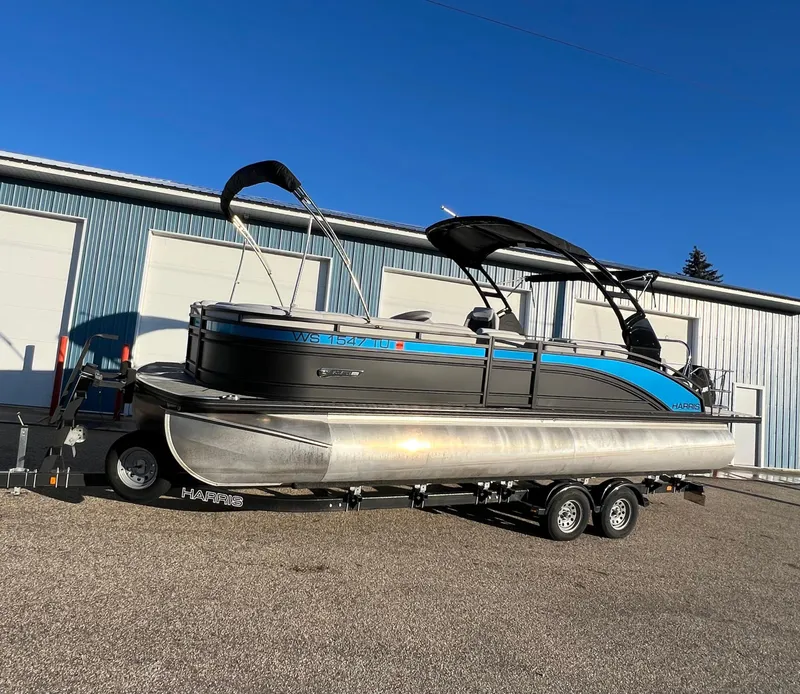 Slide: The Image of 2023 Harris Solstice 250 pontoon boat on trailer, parked outside a warehouse. - 14