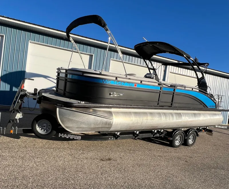 Slide: The Image of 2023 Harris Solstice 250 pontoon boat on trailer, parked outside a warehouse. - 15