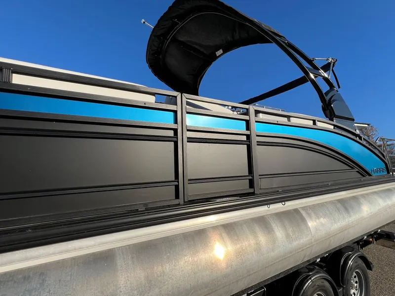 Slide: The Image of 2023 Harris Solstice 250 pontoon boat with sleek black and blue design under clear blue sky. - 18