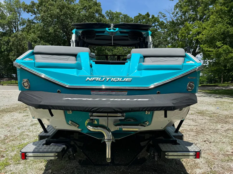 Slide: The Image of 2025 Nautique G25 boat, turquoise exterior, rear view, parked outdoors. - 12