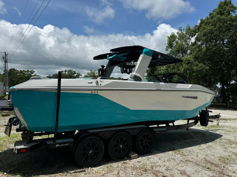 Slide: The Image of 2025 Nautique G25 boat on trailer, blue and white design, parked outdoors. - 2