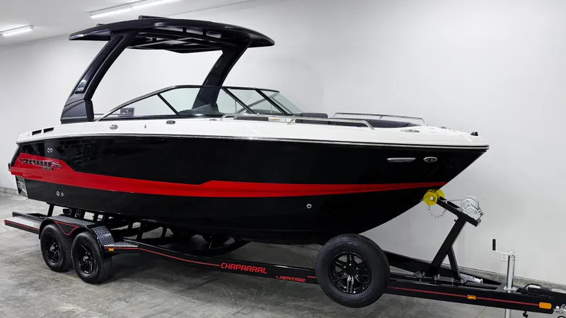 Slide: The Image of 2025 Chaparral 26 Surf boat on trailer, black and red design, in a showroom. - 2