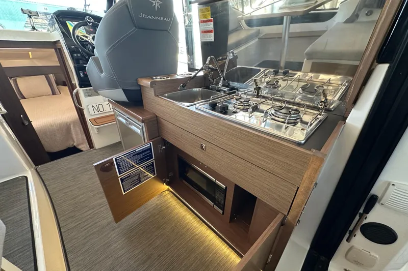 Slide: The Image of 2021 Jeanneau NC 895 interior with kitchenette, featuring stove, sink, and microwave. - 13