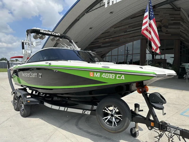 Slide: The Image of 2014 MasterCraft X2 boat on trailer, green and black design, parked near a building with an American flag. - 7