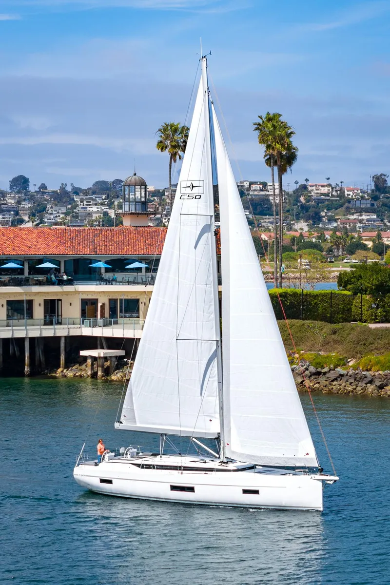 Slide: The Image of 2024 Bavaria C50 sailboat cruising near coastal buildings and palm trees. - 10