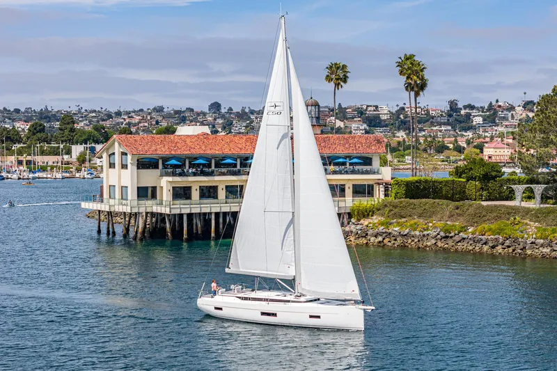 Slide: The Image of 2024 Bavaria C50 sailboat cruising near a coastal restaurant with palm trees. - 3