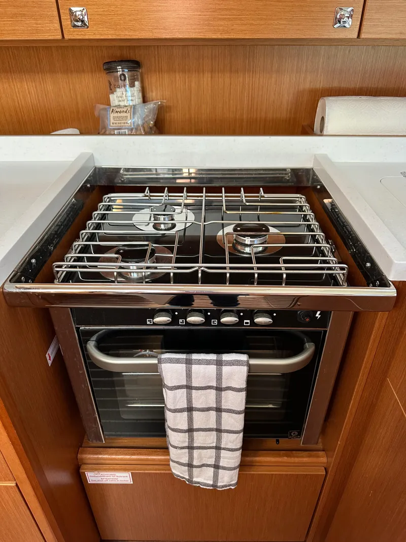 Slide: The Image of 2024 Bavaria C45 yacht kitchen with stove and oven, featuring a towel and wooden cabinetry. - 37