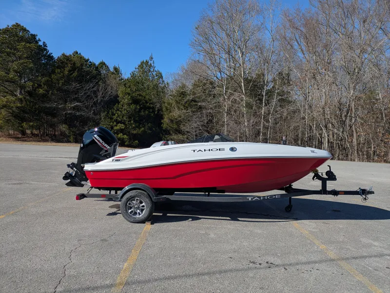 The Image of 2025 Tahoe T16 boat on trailer in parking lot, surrounded by trees. - 0