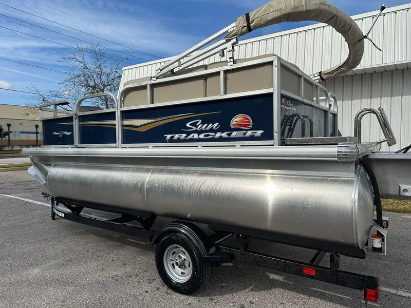 Slide: The Image of 2025 Sun Tracker Bass Buggy 16 XL Select pontoon boat on trailer, parked outdoors. - 4