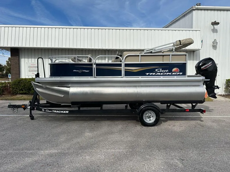 Slide: The Image of 2025 Sun Tracker Bass Buggy 16 XL Select pontoon boat on trailer, parked outdoors. - 6