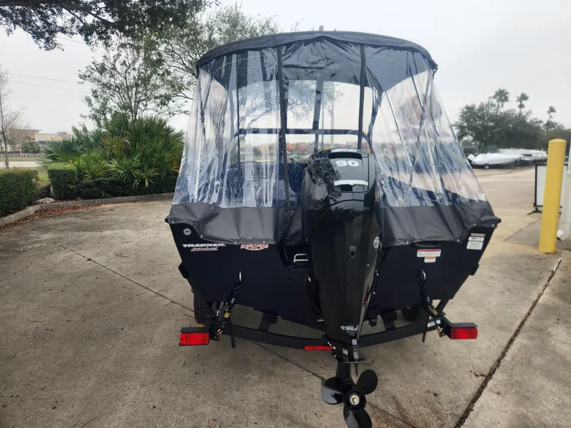 Slide: The Image of 2025 Tracker Pro Guide V-16 WT boat with canopy and motor, parked outdoors. - 5