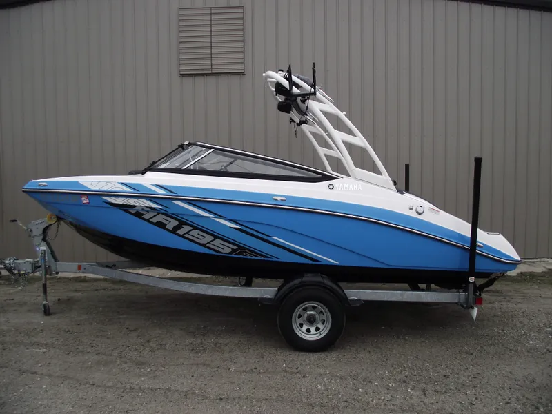 The Image of 2021 Yamaha AR195 boat on trailer, blue and white design, parked outdoors. - 0
