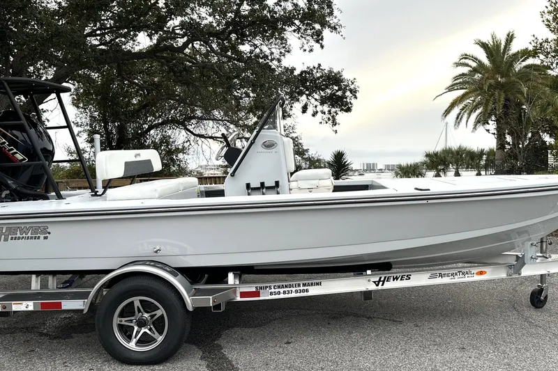 Slide: The Image of 2026 Hewes Redfisher 18 boat on trailer, parked outdoors with trees and palm in background. - 11