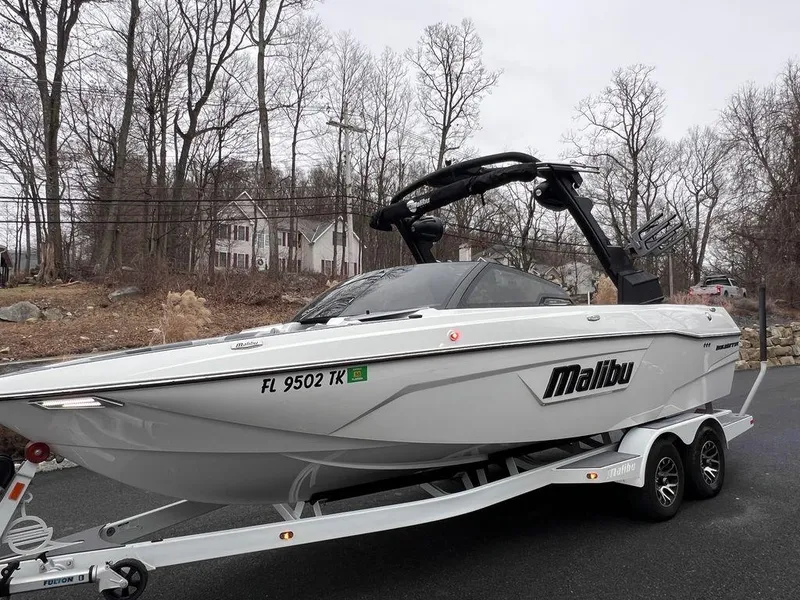Slide: The Image of 2023 Malibu 23 LSV boat on trailer, parked on a road with trees in the background. - 12