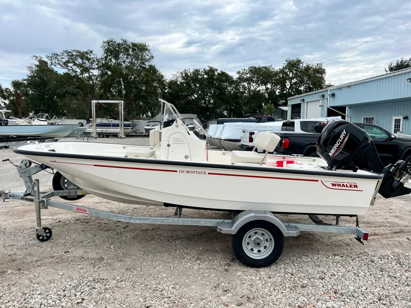 Slide: The Image of 2025 Boston Whaler 150 Montauk boat on trailer, parked outdoors. - 5