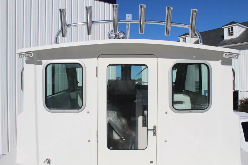 Slide: The Image of 2025 Parker 2520 boat cabin with rod holders and windows, docked near white building. - 9