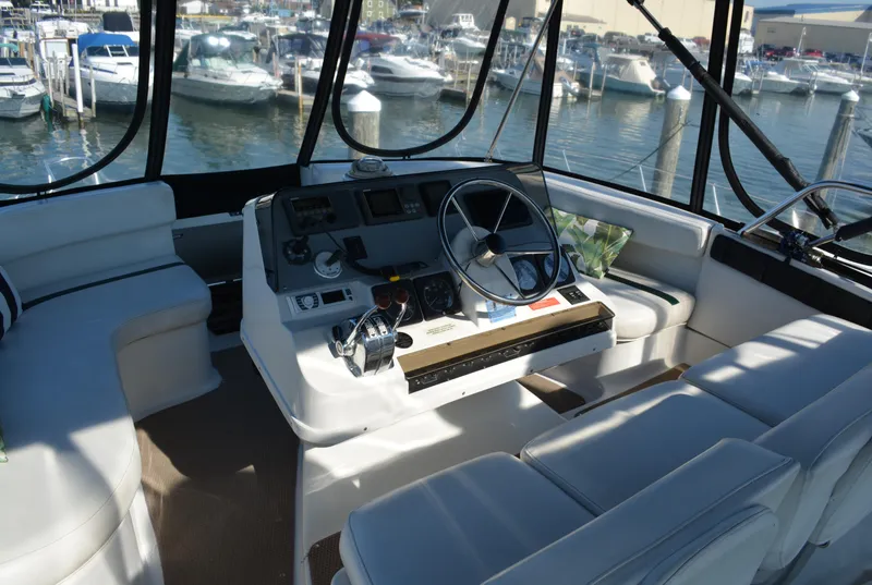 Slide: The Image of 1995 Mainship 37 Motor Yacht helm with marina view, featuring white seating and navigation controls. - 7