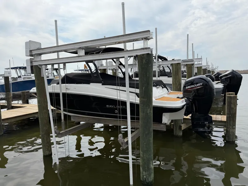 Slide: The Image of 2025 Bayliner VR5 Bowrider OB on lift at marina, featuring Mercury outboard engine. - 2
