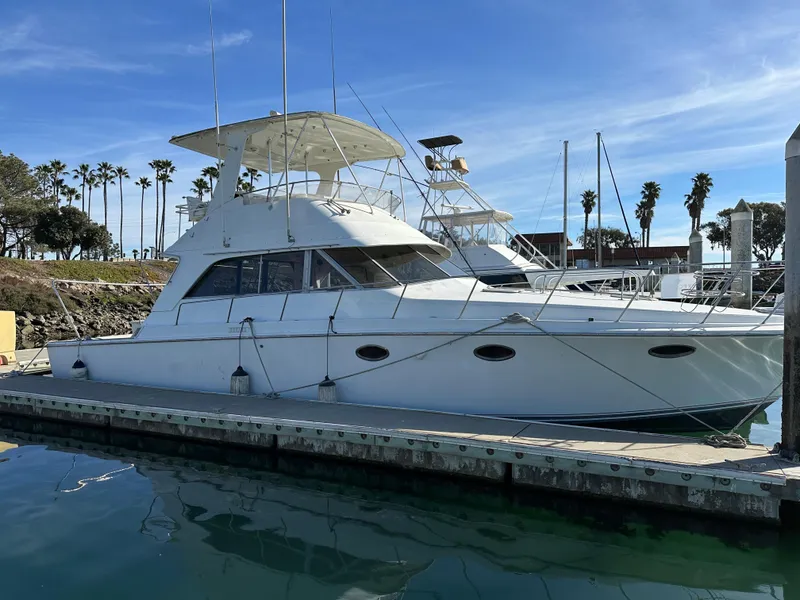 Slide: The Image of 1990 Trojan 46 Flybridge yacht docked at marina, clear sky, palm trees in background. - 30