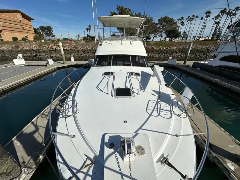 Slide: The Image of 1990 Trojan 46 Flybridge yacht docked at marina, clear sky, palm trees in background. - 35