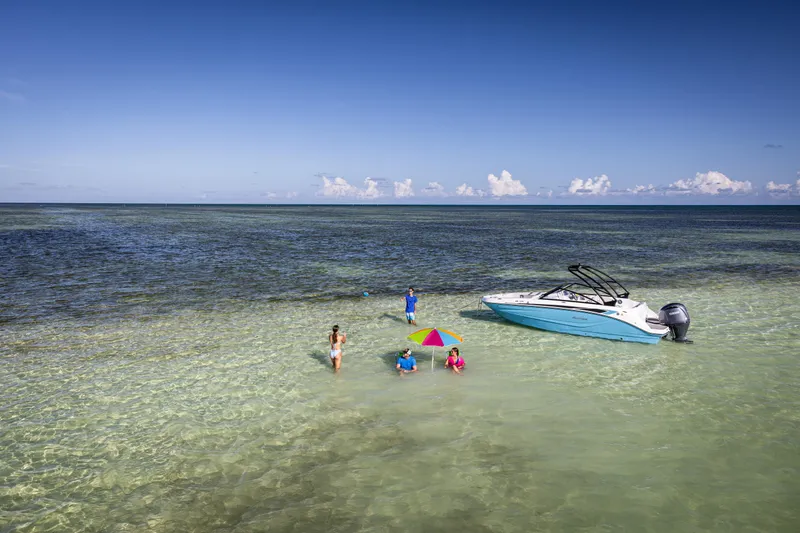 Slide: The Image of 2025 Hurricane SunDeck 235 OB boat anchored in shallow, clear water with people relaxing nearby. - 34