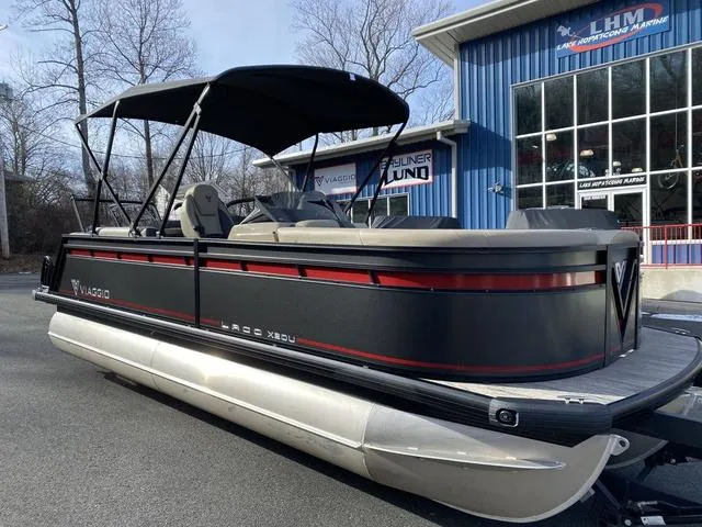 Slide: The Image of 2025 Viaggio x20u pontoon boat with canopy, parked near a blue building. - 2