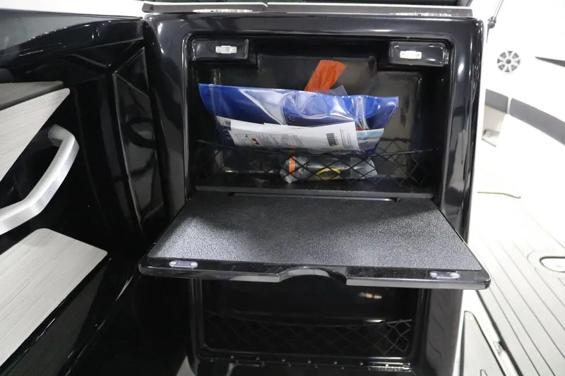 Slide: The Image of 2025 Yamaha Boats 222S storage compartment with open shelf and netted pocket. - 13