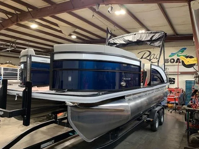 Slide: The Image of 2025 Harris Cruiser 210 pontoon boat in a showroom, featuring sleek design and modern amenities. - 1