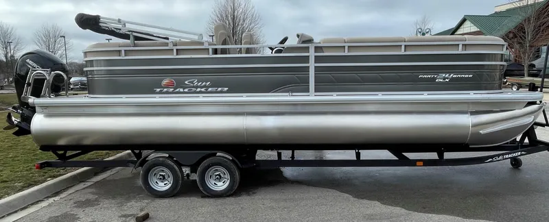 The Image of 2025 Sun Tracker Party Barge 24 DLX pontoon boat on trailer, parked outdoors. - 0