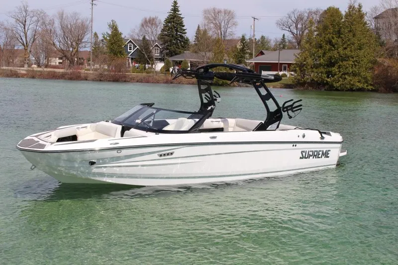 Slide: The Image of 2025 Supreme S220 boat on a serene lake with trees and houses in the background. - 1