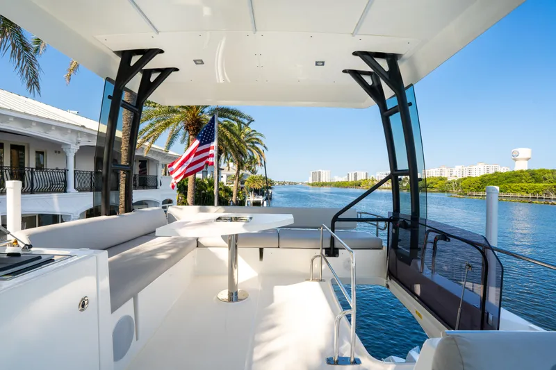 Slide: The Image of Prestige 460 Fly 2023 yacht deck with seating, table, and American flag, overlooking waterfront. - 15