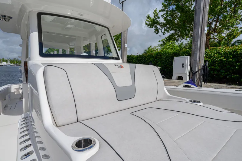 Slide: The Image of 2023 SeaVee 420Z boat with cushioned seating and cup holders, docked by lush greenery. - 7