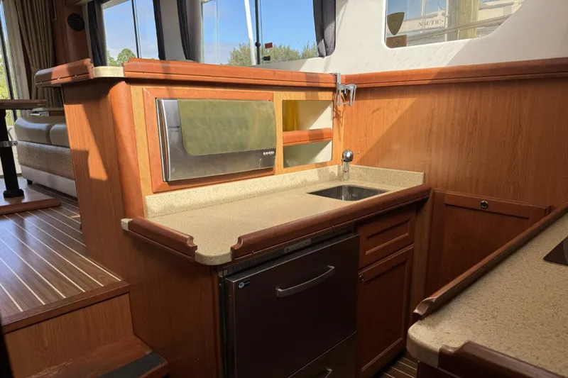 Slide: The Image of 2008 Mainship 34 Trawler Hardtop interior with kitchenette, featuring wood cabinetry and modern appliances. - 16