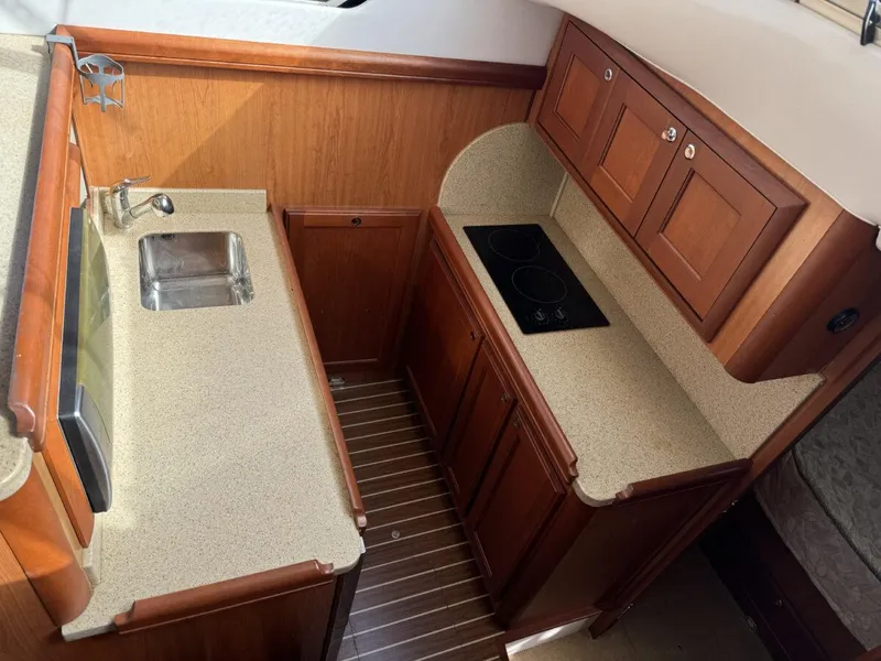 Slide: The Image of 2008 Mainship 34 Trawler Hardtop galley with sink, stove, and wooden cabinetry. - 17