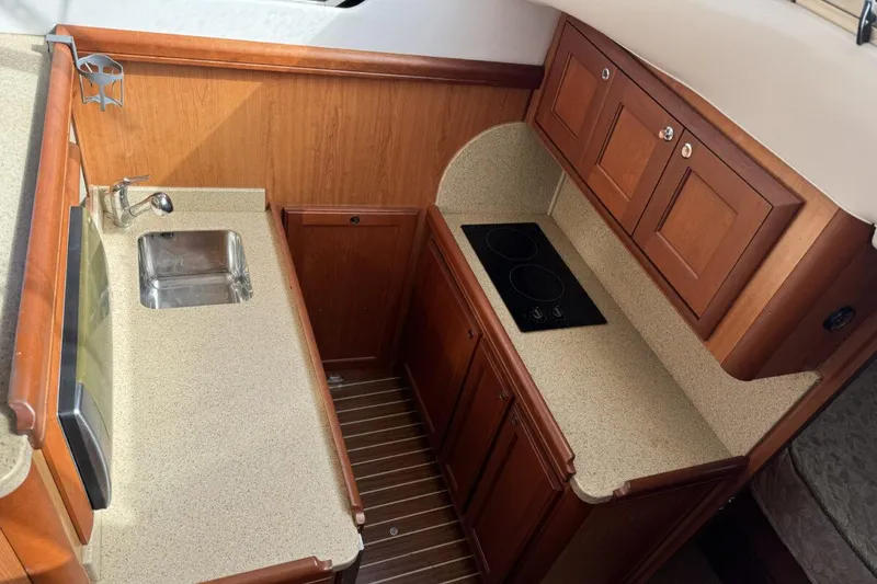 Slide: The Image of 2008 Mainship 34 Trawler Hardtop galley with sink, stove, and wooden cabinetry. - 18