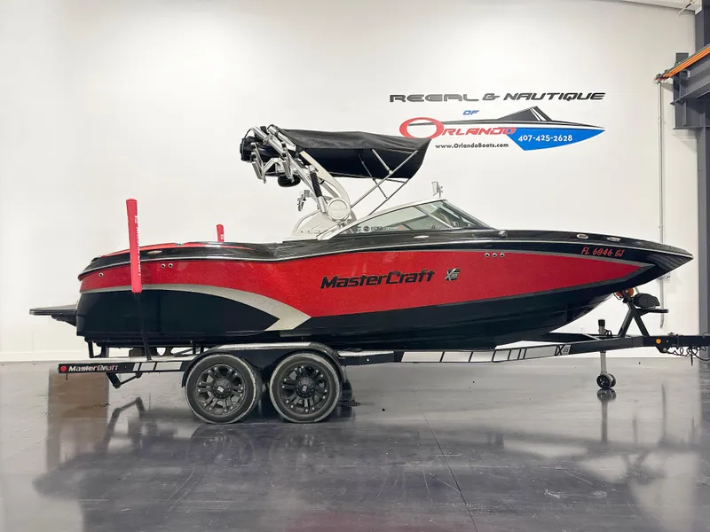 The Image of 2015 MasterCraft X23 boat in showroom, red and black design, on a trailer. - 1