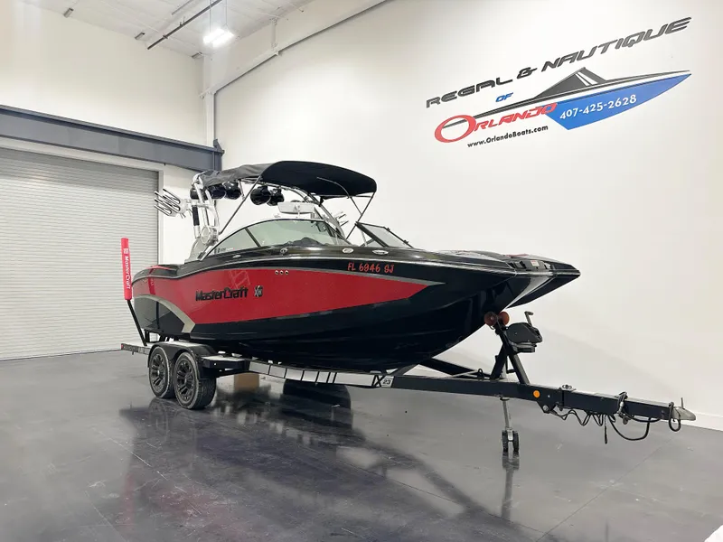 Slide: The Image of 2015 MasterCraft X23 boat in showroom, black and red design, on trailer. - 2