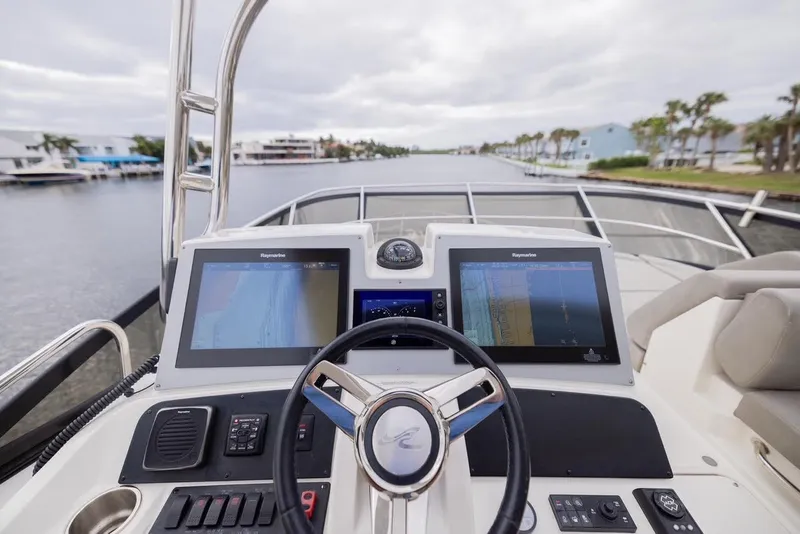Slide: The Image of 2017 Sea Ray 59 Flybridge helm with dual navigation screens on a calm waterway. - 8