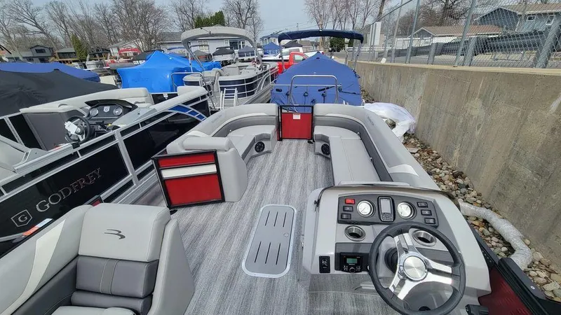 Slide: The Image of 2025 Bennington 24 SXSB pontoon boat with modern seating and control panel, docked among other boats. - 5