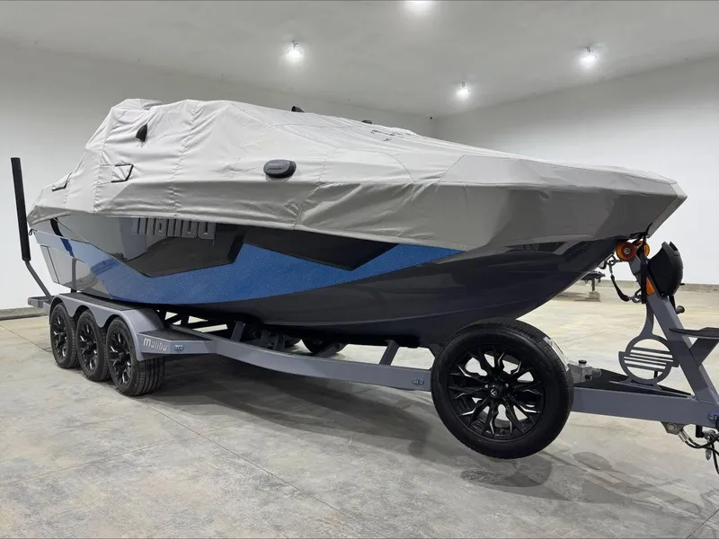 Slide: The Image of 2024 Malibu M242 boat covered on a trailer in a well-lit garage. - 6