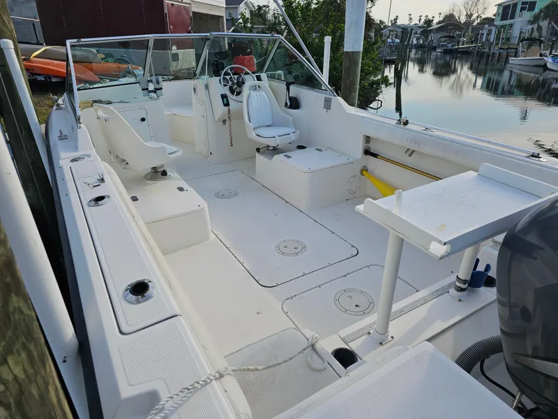 Slide: The Image of 1994 Pursuit 2150 DC boat interior, featuring seating and steering wheel, docked by calm waters. - 2