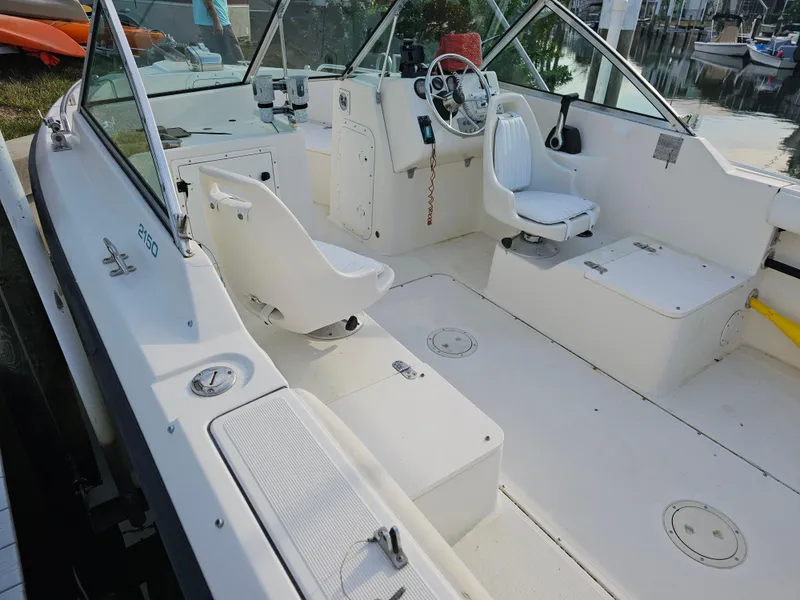Slide: The Image of 1994 Pursuit 2150 DC boat interior with white seating and steering wheel, docked by the water. - 3