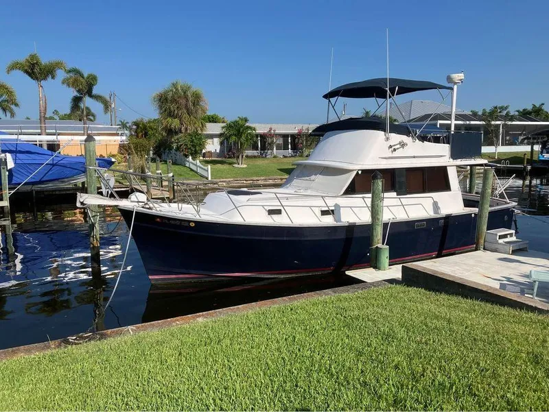 The Image of 1981 Mainship 34 Trawler docked by lush green lawn and palm trees. - 0