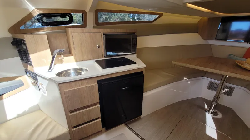 Slide: The Image of 2023 NX Boats NX340 interior with kitchenette, featuring sink, stove, and seating area. - 15