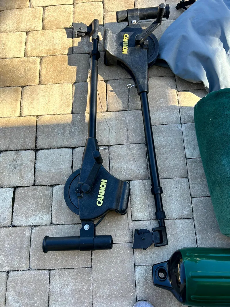 Slide: The Image of Cannon downriggers on a brick patio, near a 2003 Pursuit 2470 Center Console boat. - 8